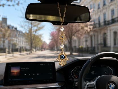 Gold Hamsa hand and blue evil eye car charm hanging from a BMW rear-view mirror on a sunny London street – THE AURA CO.