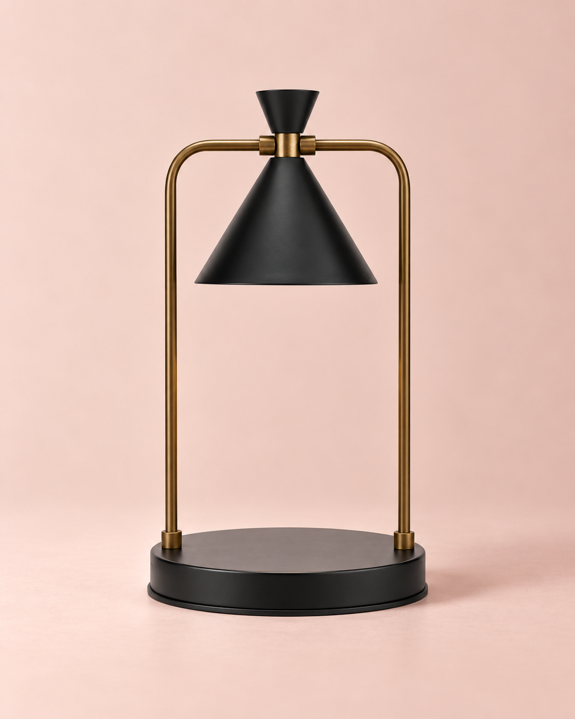 Black candle warmer lamp with gold-tone curved frame and round black base against a blush-pink background