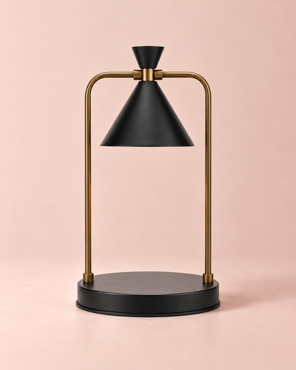 Black candle warmer lamp with gold-tone curved frame and round black base against a blush-pink background