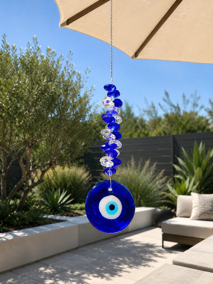 Cobalt blue glass evil eye sun catcher hanging under a garden parasol in a sunny outdoor setting – THE AURA CO.