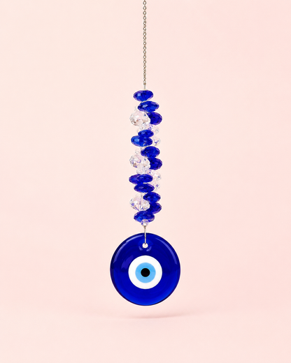 Cobalt blue glass evil eye sun catcher with blue and clear crystal beads on a silver chain on a blush pink background – THE AURA CO.