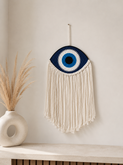 Cream macramè evil eye wall hanging with long fringe styled on a white wall with dried pampas grass – THE AURA CO.